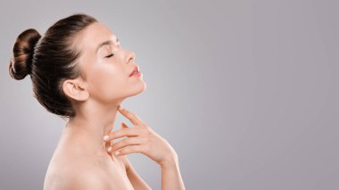 Gözleri kapalı, boynuna dokunan, gri arka planı olan bir kadın.