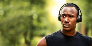 Kablosuz kulaklıklı, parktaki eğitimli, boş alana bakan konsantre siyahi adamın portresi.