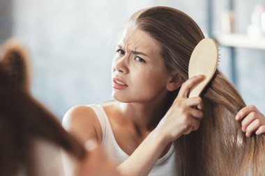 Hüsrana uğramış genç bir kadın banyoda aynanın önünde karışık saçlarını taramaya çalışıyor.