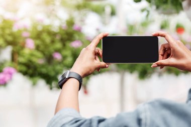 Serada aletlerle çalışmak. Afrika kökenli Amerikalı kız elinde boş ekranlı akıllı telefon, renkli çiçekler, bulanık arka plan, kesilmiş