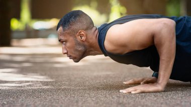 Açık havada çalışan kaslı siyahi adamın yan görüntüsü, parkta şınav çekerken. Panorama