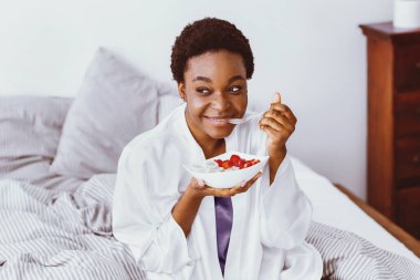 Sağlıklı kahvaltı. Gülümseyen Afrikalı Amerikalı kız elinde bir tabak yulaf ezmesi ve meyve tutuyor.