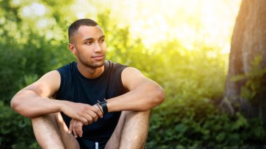 Yakışıklı Afro-Amerikan sporcu yolda oturuyor, parktaki eğitiminden sonra mola veriyor. Panorama