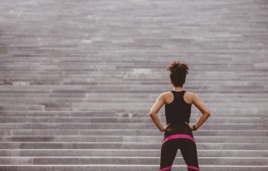 Sıkı çalışmaya başla. Spor giyimli Afro-Amerikan atletik Afrikalı kız büyük gri şehir merdivenlerine bakıyor, geri, serbest alan