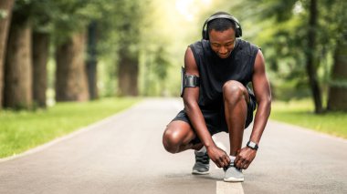 Parkta koşmadan önce bağcıklarını bağlayan Afrikalı bir adam.