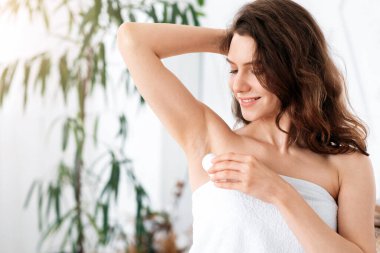 Havluya sarılı güzel bir kadın yatak odasında deodorant kullanıyor.