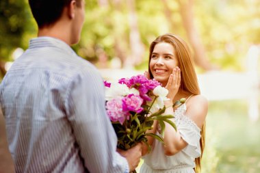 Sevecen genç bir adam kız arkadaşına dışarıda çiçek buketiyle sürpriz yapıyor.