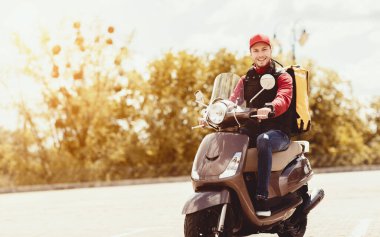 Kurye, şehrin dışında sarı sırt çantasıyla motosikletle yiyecek getiriyor. Yemek dağıtım servisi. Boşluğu Kopyala