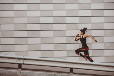 Hızlan ve kaç. Spor giyimli Afro-Amerikan atletik kız, gri duvarlı arka planda, serbest alanda koşuyor.