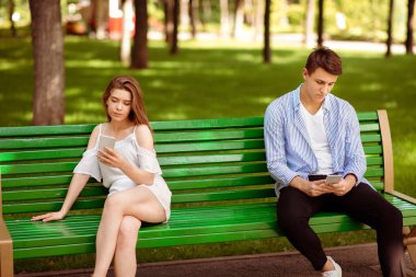 Gadget bağımlılığı ve ilişki sorunları. Milenyum çifti akıllı telefonları parktaki bankta oturuyor, birbirlerini görmezden geliyorlar.