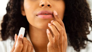 Dudak kremi. Tanımlanamayan siyah kadın dudaklarına nemlendirici ruj sürüyor, kırpılmış görüntü, yakın plan.