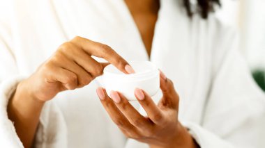 Duştan sonra cildini nemlendirmek için ellerinde organik krem olan tanınmamış siyah bir kadın.