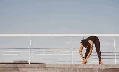 Açık havada yaz sporu. Spor kıyafetleri içinde Afrikalı Amerikalı bir kız mavi gökyüzü arka planında stadyumda spor yapıyor ve egzersiz yapıyor.
