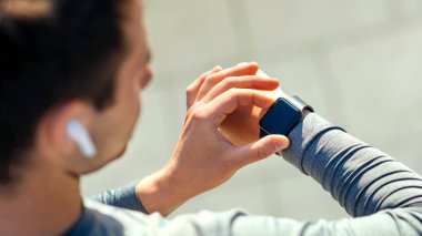 Kullanışlı aletlerle modern çalışma. Kablosuz kulaklıklı adam, durup takip cihazını kontrol ediyor, omuzdan görüyor, boş alan var.