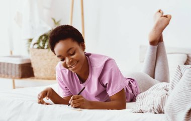 Günlük tut, düşüncelerini yaz ve evde fikirler yarat. Rüyamda gülümseyen, Afro-Amerikan güzel bir bayan yatakta oturuyor ve deftere kalemle yazıyor, yatak odasının içinde, fotokopi odasında.