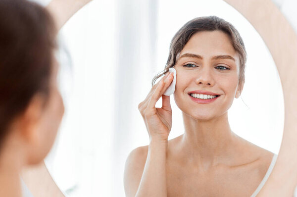 Fresh girl looking at mirror and using cotton pad, cleamsing morning procedures at home