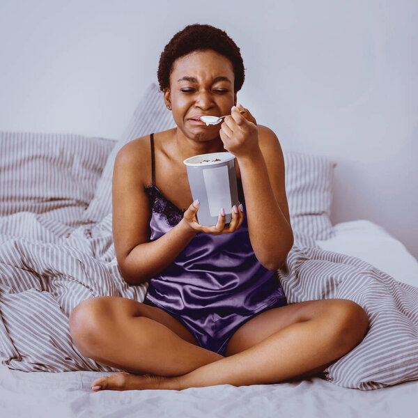 Breakup and sadness concept. Crying african american girl eating ice cream in bed at home