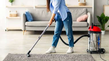 Modern bir evde, genç bir kadın özenle dokunmuş bir halıyı süpürüyor. Günlük giysiler giyiyor ve parlak ve serin oturma odasında düzenli bir yaşam alanı kurmaya odaklanıyor..