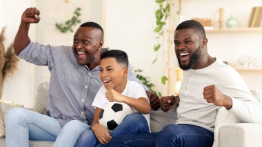 Üç kişilik neşeli bir aile futbol maçı izlerken coşkuyla tezahürat yapıyor. Oturma odalarında rahatça oturuyorlar, oyun için heyecan ve beklentiyle dolu..