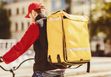 Yemek teslimatı. Tanınmayan Kurye, şehirde bisiklete binen sarı sırt çantasıyla yiyecek getiriyor. Seçici Odaklanma