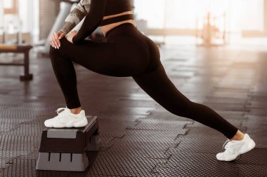 Bir insan spor salonunda derin bir esneme hareketi yapar, bir ayağını spor salonuna koyar ve yoğun bir antrenmana hazırlanır. Çevre aydınlık ve uygunluğa odaklı..