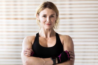 Spor, sabah egzersizi, antrenman kasları, vücut egzersizi, sağlıklı yaşam tarzı. Cana yakın, çekici, kaslı, spor giyimli olgun bir kadın. İz sürücü kollarını göğsüne bağlamış ve kameraya bakıyor.