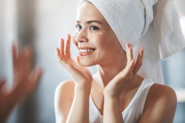 Evdeki aynanın yanında duş aldıktan sonra gözlerinin altına krem süren güzel bayan.