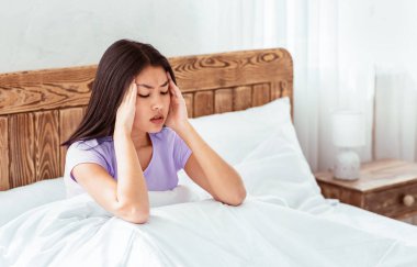 Çinli bir kadın migren ağrısı çekiyor. Baş masajı yapıyor. Evde yatakta oturuyor. Boş Alan