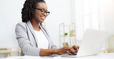 CEO 'su Afrikalı Amerikalı genç bir kadın laptopta iş e-postaları yazıyor, işyerinde oturuyor, dizüstü bilgisayarında daktilo yazıyor.