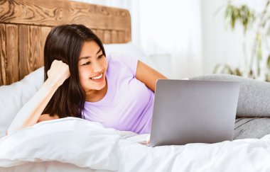 Mutlu Asyalı kız dizüstü bilgisayar kullanıyor hafta sonu sabahı evde internette internette geziniyor..