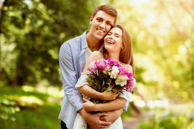 İlk yıldönümü hediyesi. Millennial evli çiftler bir buket çiçekle parkta sarılıyorlar.