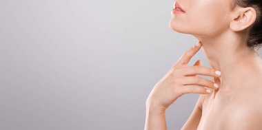 Gözleri kapalı, boynuna dokunan, gri arka planı olan bir kadın.