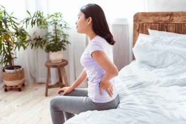 Sırt ağrısı kavramı. Asyalı kadın evde yatağında sırt üstü yatarken acı çekiyor..