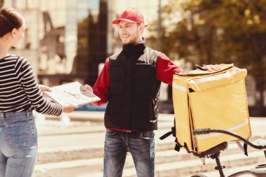 Hızlı Teslimat Kurye Servisi. Dışarıdaki bisikletli kıza kâğıt paketi veren adam. Şehir merkezinde bisikletli bir kız. Seçici Odaklanma