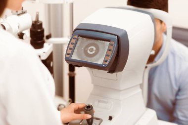 Bir tıbbi uzman görüş sağlığını değerlendirmek ve hastaların gözlerinde mevcut olan sorunları tespit etmek için teşhis ekipmanları kullanırken, bir hasta göz muayenesinden geçirilir..