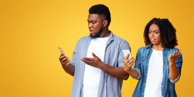 Bir erkek ve bir kadın akıllı telefonlarını kontrol ederken bir anlık bir inançsızlık sergilerler. Duygusal tepkileri parlak sarı arka plan tarafından vurgulanır..