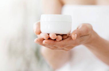 Tanınmaz haldeki kadın duş aldıktan sonra havluya sarılmış krema kavanozu, vücut bakımı konsepti, boş yer.