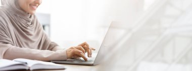 Ofiste dizüstü bilgisayarda çalışan, klavyede yazan ve gülümseyen, boş alan ile kırpılmış resimli tanınmamış Müslüman kadın.