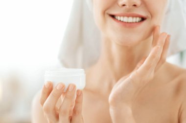 Evde duştan sonra yüz kremi süren genç bir kadın.