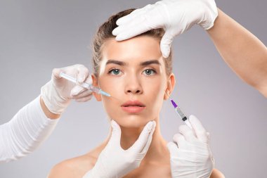Modern güzellik kavramı. Çekici genç bir kadın kozmetoloji kliniğinde tedavi görüyor. Güzel genç bayan için güzellik iğneleri yapan güzeller, yakın plan, gri stüdyo arka plan, kopyalama alanı