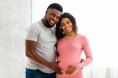 Genç, evde poz veren Afrikalı bir çift bekliyor. Pencerenin yanında duruyorlar ve gülümsüyorlar.