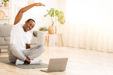 Spor dersleri çevrimiçi. Genç siyah adam evde geriniyor, dizüstü bilgisayar kullanıyor, boşluğu kopyalıyor.