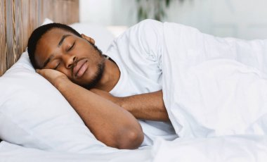 Uyuyan Afrikalı Amerikalı adam evinde rahat yatağında huzur içinde uyuyor, gözleri kapalı yatıyor. Dinlenme, derin erkek uykusu, dinlenme ve uyku konsepti.