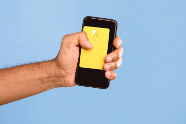 Genç bir Afrikalı Amerikalı, elinde sarı bir kartla akıllı telefonu tutarken kendini aydınlık bir ortamda soyutluyor. O anın basitliği modern yaşam tarzı seçimlerini vurguluyor..