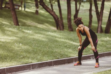 Koşarken nefes al. Spor kıyafetli, spor ayakkabılı, kulaklıklı, yorgun Afrikalı Amerikalı kız Green Park 'ta durdu.