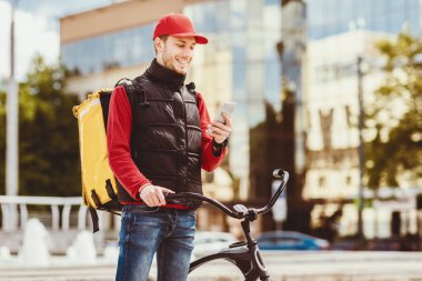 Yemek teslimat servisi. Kurye, cep telefonunu kullanarak dışarıdaki bisikletli restoranlardan yiyecek getiriyor. Boş Alan