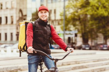 Kurye Servisi. Bisikletli teslimatçı, şehirde bisikletli poz verirken kameraya gülümsüyor. Metin için Boşluk