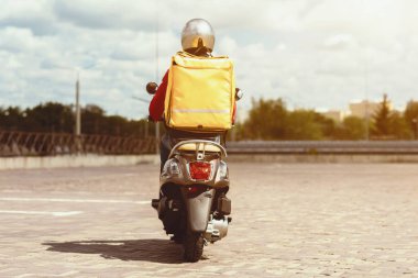 Fast Food Teslimatı. Kurye Scooter 'a biniyor. Dışarıdaki sarı çantalı restoranlardan yemek getiriyor. Geri Görünüm, Uzayı Kopyala