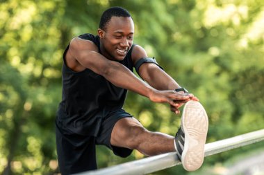 Genç Afrikalı bir adam halka açık parkta egzersiz yapıyor, vücudunu esnetiyor.