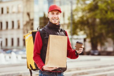 Yemek teslimatçısı. Kahve ve kağıt pakette yemek teslimatı. Sarı sırt çantasıyla şehir merkezine gidiyor..